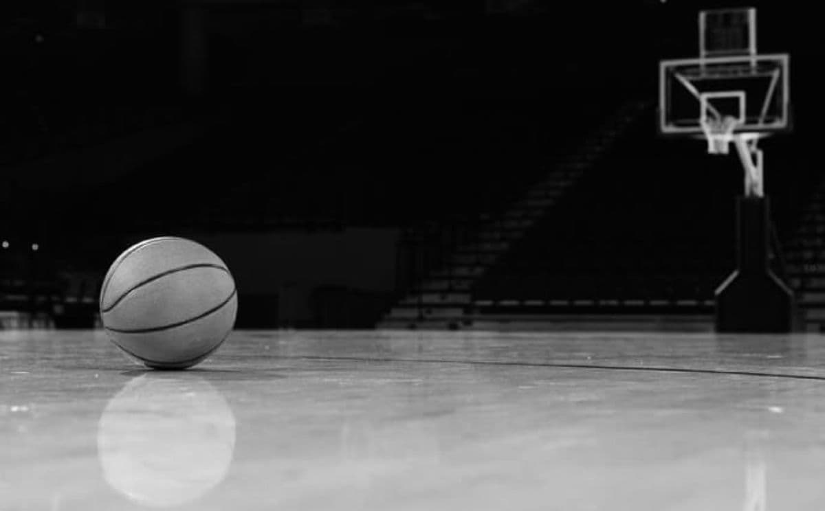 An empty basketball court with a ball lying on the floor and the net visible in the background.